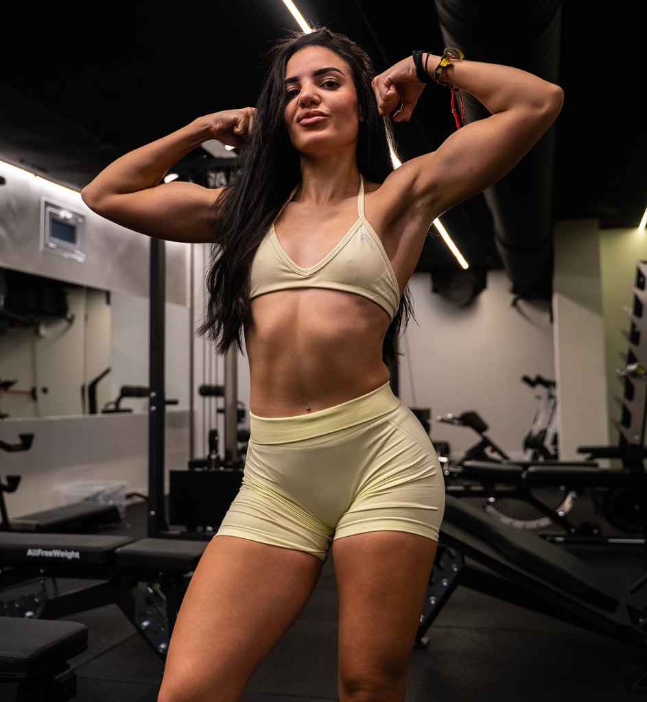 El entrenadora está posando en el gimnasio con un atuendo deportivo amarillo.