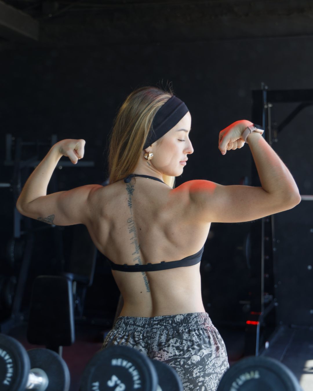 La coach flexiona los bíceps de espaldas en un gimnasio.