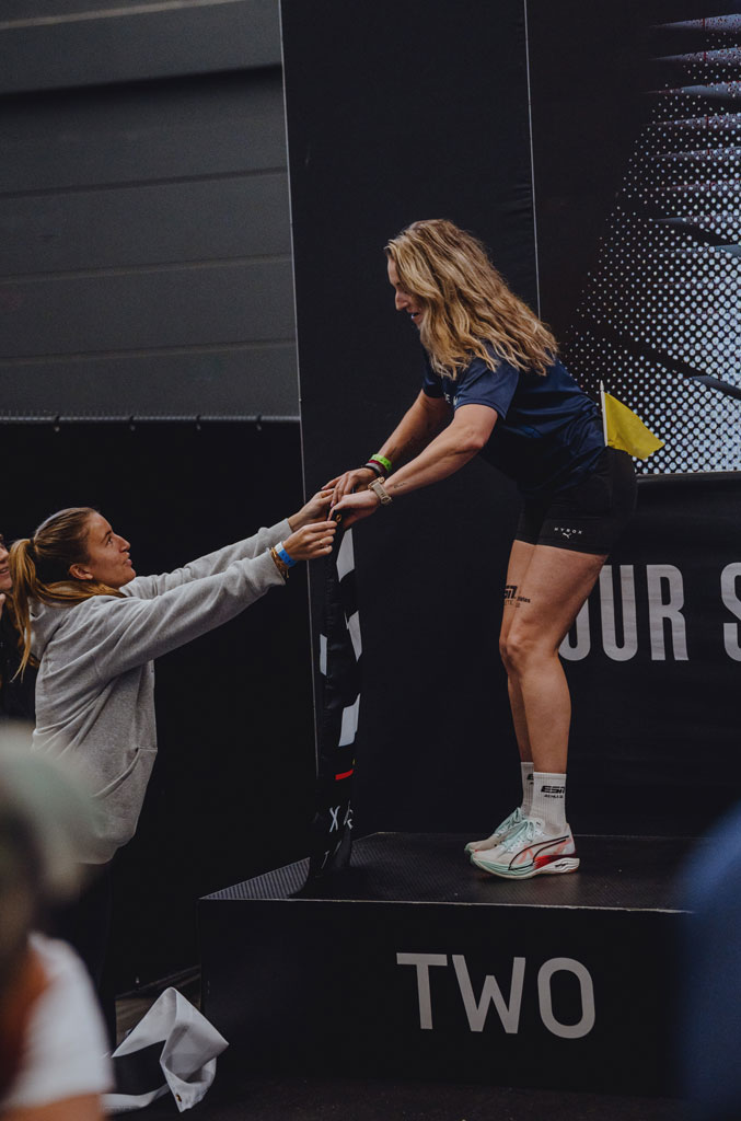 Een coach op een podium wordt geholpen door een vrouw tijdens een fitnessevenement.
