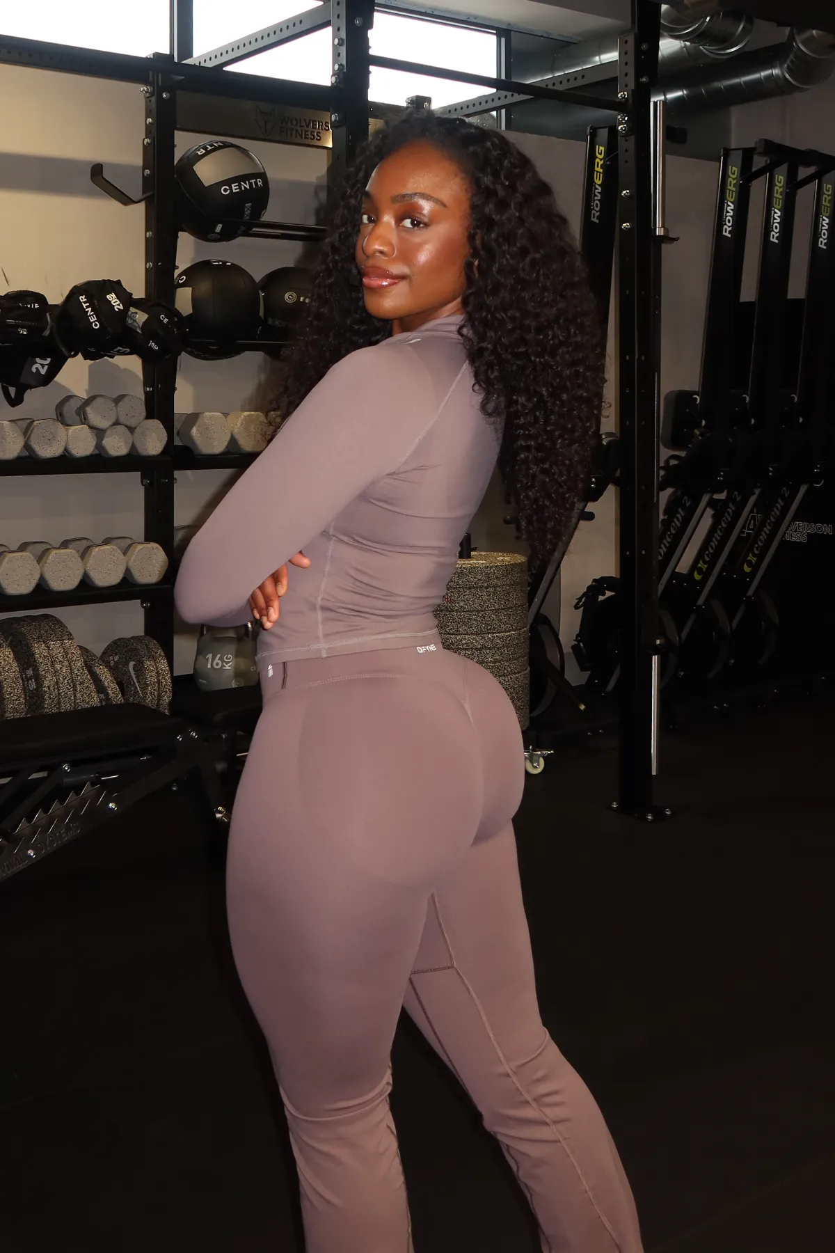 The coach poses in a gym, looking back over her shoulder.