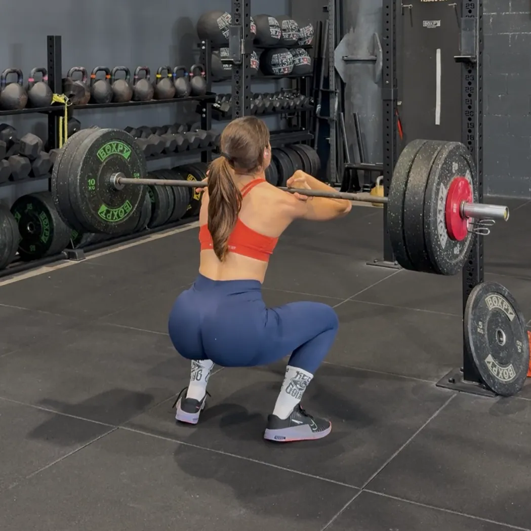 La coach hace una sentadilla con barra en el gimnasio.