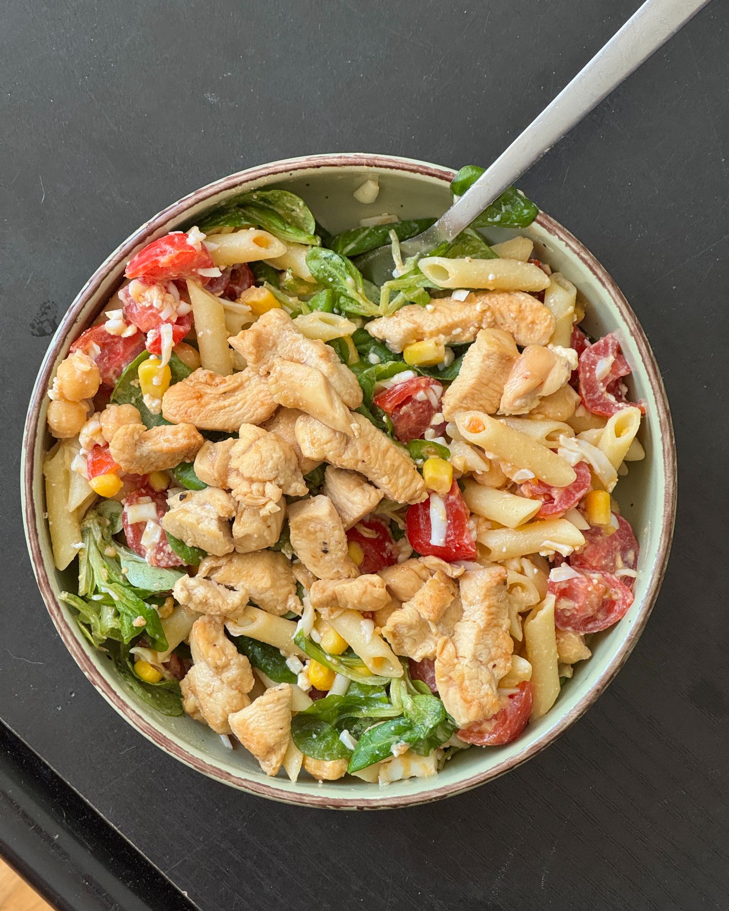 Un bol de ensalada de pasta con pollo, tomate y maíz.