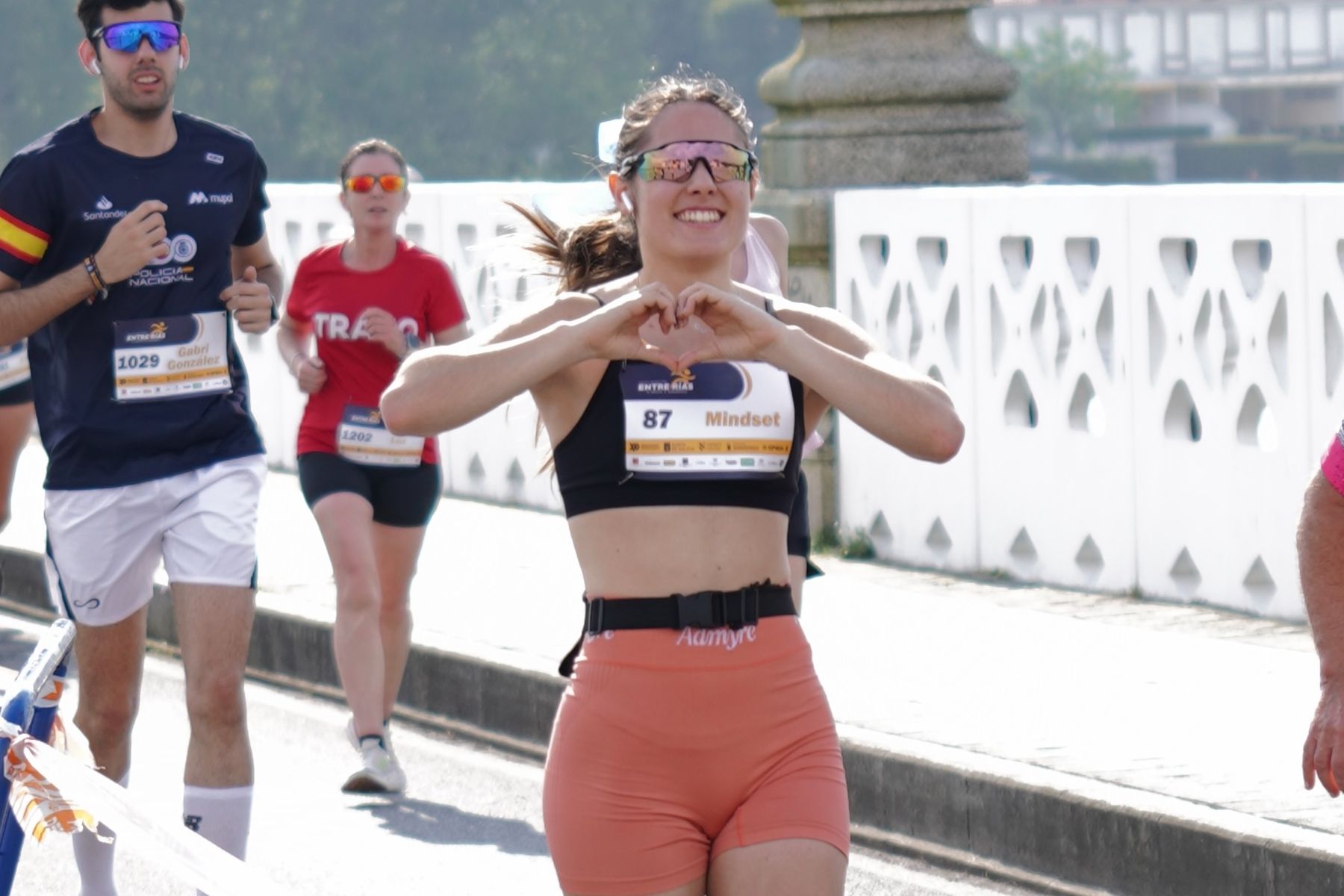La coach corre una carrera haciendo un corazón con las manos.