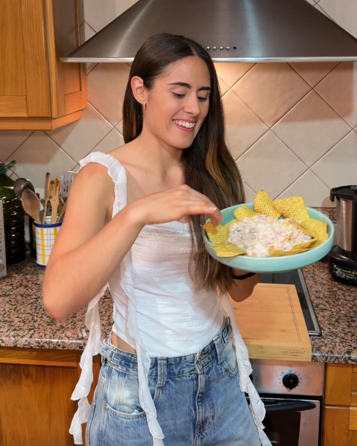 La coach sonríe en la cocina con un plato de nachos.