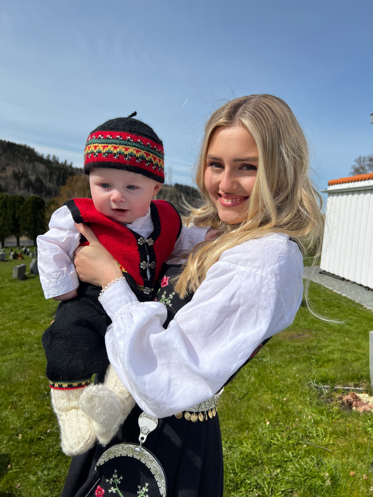 Treneren poserer utendørs med babyen sin.