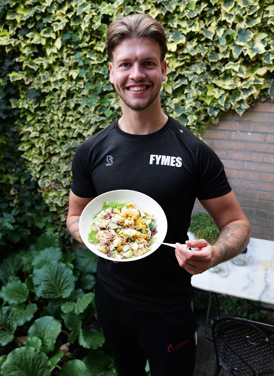 De coaching staat buiten met een bord gezond eten in de hand.